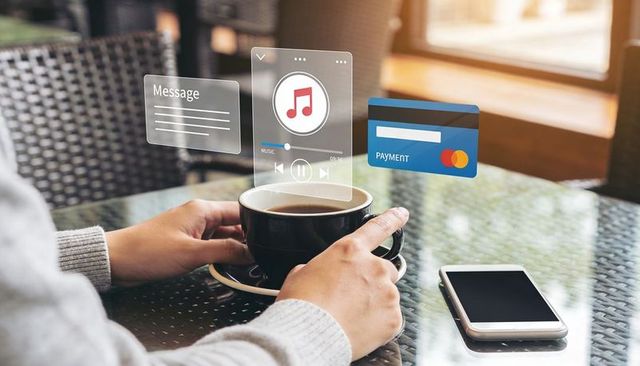 Hands Holding Coffee Cup with Holographic Payment and Music Interface on Glass Table
