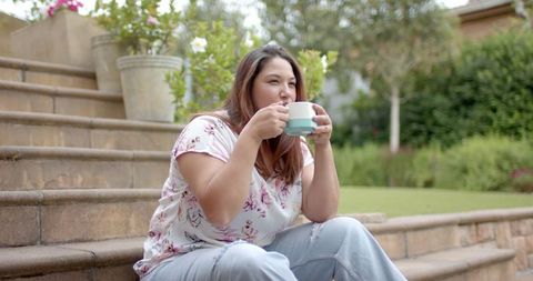 Content Woman Enjoying Coffee Outdoors on Garden Steps