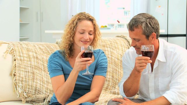 Spending a relaxing evening indoors, a couple savors red wine while sharing a comfortable moment on the sofa. This scene is perfect for illustrating concepts of relaxation, home life, and togetherness. Ideal for use in lifestyle blogs, home decor sites, or advertisements promoting a cozy and intimate atmosphere.