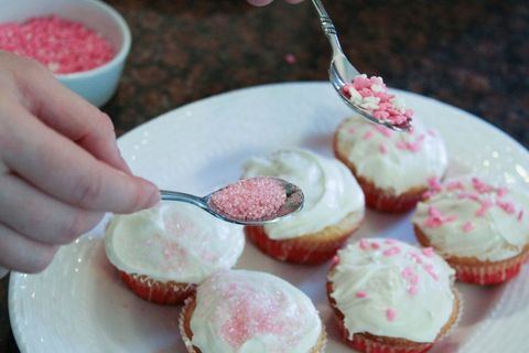 Hand decorating homemade cupcakes with pink sprinkles