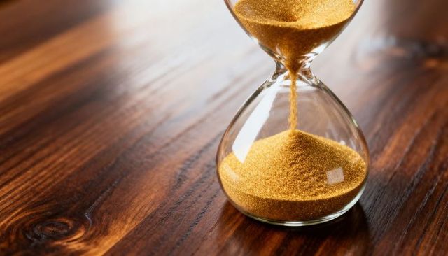 Pouring golden hourglass sand on polished wood surface, time passing concept