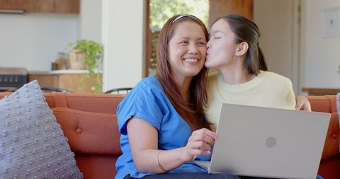 Asian Mother and Daughter Bonding on Cozy Sofa with Laptop