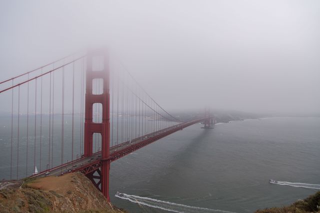 Golden Gate Bridge partially covered in morning fog, stretching over San Francisco Bay. Great for content related to travel, tourism, San Francisco attractions, iconic landmarks, coastal scenery, California images, architectural marvels, and atmospheric conditions.