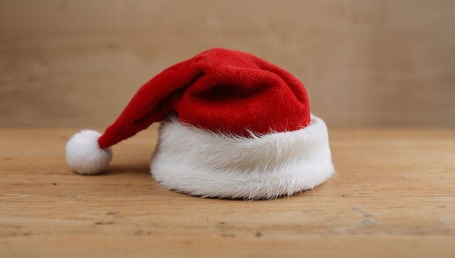 Red Velvet Santa Hat with Fluffy White Fur Trim and Pom-Pom on Wooden Table