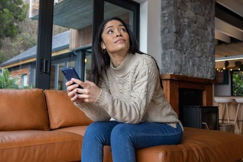 Young woman using smartphone on caramel leather sofa in cozy modern living room