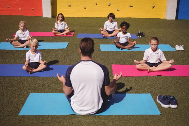 Coach leading group of schoolchildren in yoga session on colorful mats in schoolyard. Children practicing meditation and mindfulness, promoting physical fitness and mental well-being. Ideal for educational materials, health and wellness campaigns, and promoting children's activities.