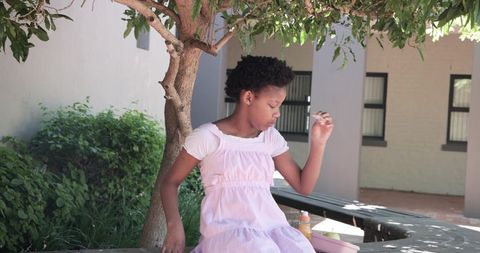 African american teen girl sitting in school courtyard holding snack beside pink lunchbox