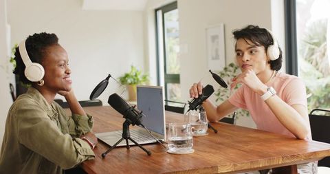 Diverse co-hosts recording podcast at home studio with microphones, laptop, headphones