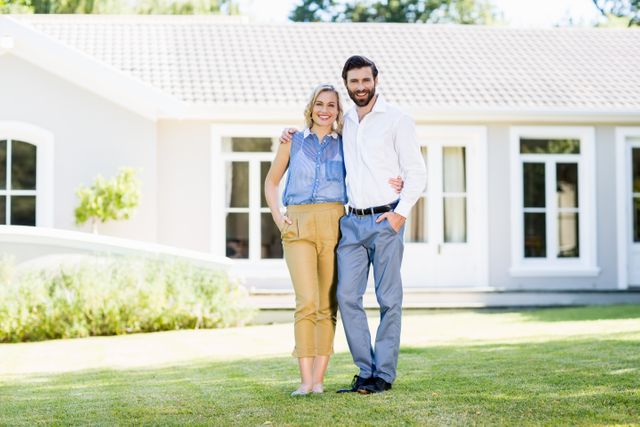 Happy couple standing in the garden of a modern home, smiling and embracing. Ideal for use in real estate promotions, lifestyle blogs, family-oriented advertisements, and homeownership articles.