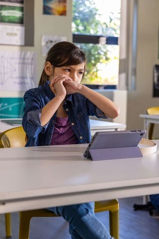 Asian schoolgirl using tablet raising hand in modern classroom focused learning moment