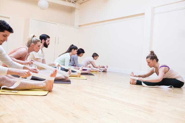 Trainer assisting group of people with stretching exercise in the fitness studio