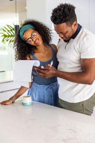 Young couple checking phone and receipt while leaning on bright modern kitchen island