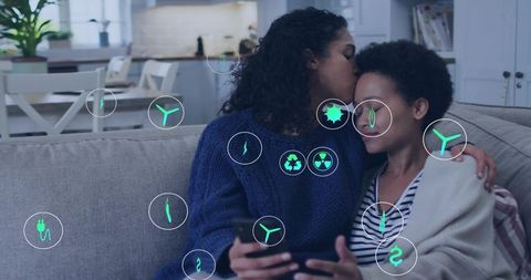 Kissing couple on couch sharing device showing eco technology icons in open-plan living room
