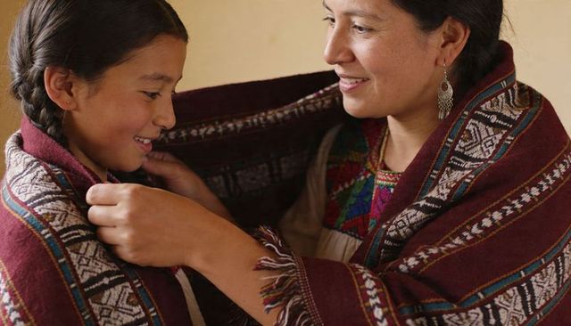 Mother wrapping daughter in traditional woven shawl sharing warmth and care