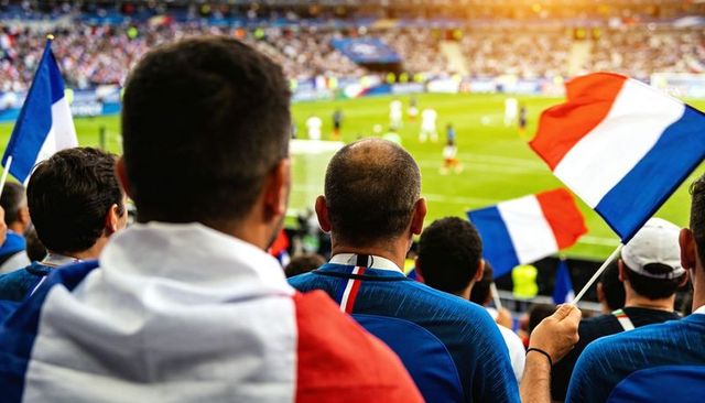 Bald fan cheering and waving french tricolor flag in packed football stadium crowd