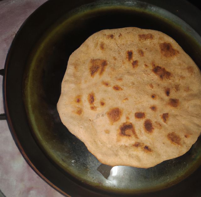 Indian chapati being prepared in a cast iron pan on a gas stove. Chapati or 'roti' is a traditional Indian flatbread made from wheat flour. This photo can be used in articles or blogs relating to Indian cuisine, cooking tutorials, healthy homemade recipes, traditional culinary practices, or cultural spreads.