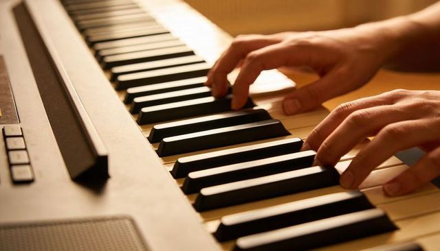 Pianist hands playing digital keyboard in warm studio light, closeup