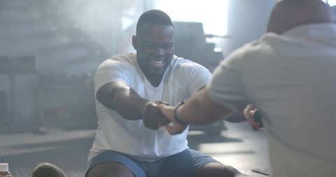 African man smiling while gripping hands with partner, pushing teamwork during gym workout