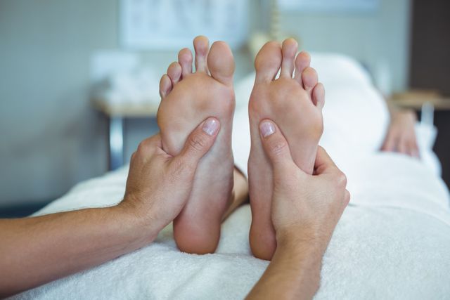 Close-up of physiotherapist's hands massaging a woman's feet in a clinical setting. Ideal for use in articles or advertisements related to wellness, healthcare, physiotherapy, and relaxation treatments. Can be used to promote spa services, medical clinics, or therapeutic practices.