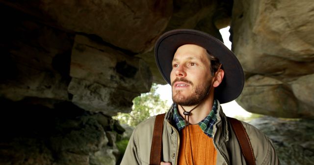 Happy caucasian man in hat trekking on rocky mountainside exploring cave, copy space. Exploration, adventure, hiking, nature, hobbies, healthy lifestyle and outdoor activities, unaltered.