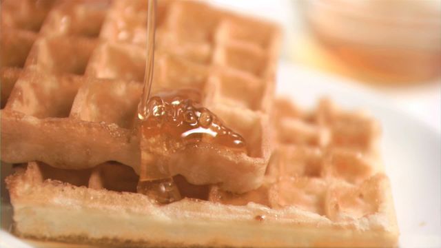 Golden honey slowly drizzling over crisp waffles, highlighting the delicious texture and richness. Perfect for use in culinary blogs, breakfast recipe collections, or advertisements focused on sweet treats and morning meals.