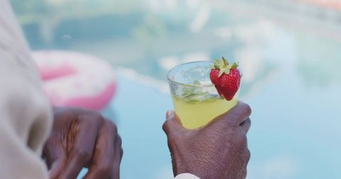 Mature african american man holding yellow cocktail with strawberry mint garnish by pool