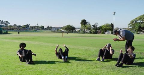 Coach leading sit-ups on cricket field during outdoor fitness training session