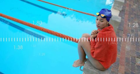 Competitive Swimmer Sitting on Pool Edge Wrapped in Red Towel Wearing Blue Cap and Goggles