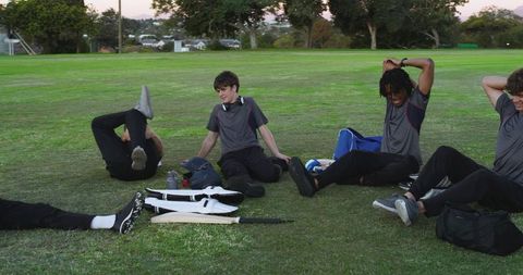 Teen teammates stretching together on grassy cricket field before training session, sports teamwork