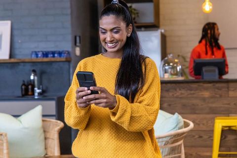 Young woman texting and smiling in cozy rustic cafe wearing mustard sweater