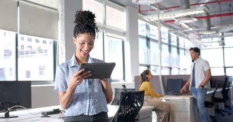 Young professional using tablet in bright open-plan office with colleagues collaborating