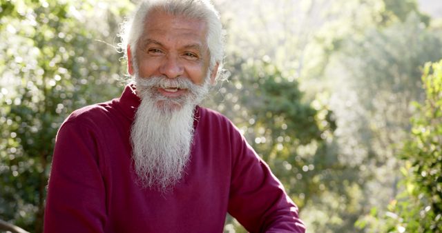 Portrait of senior biracial man with white beard smiling in sunny nature, copy space, slow motion. Summer, retirement, wellbeing and healthy senior lifestyle, unaltered.