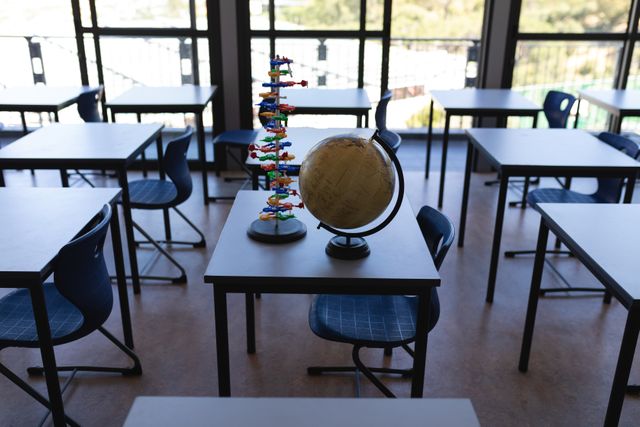 Surface level of a globe and a DNA model immobile on a table in an empty classroom