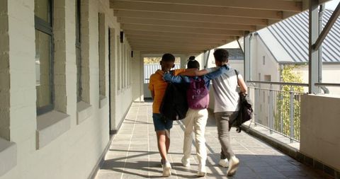 Friends embracing while walking in school corridor