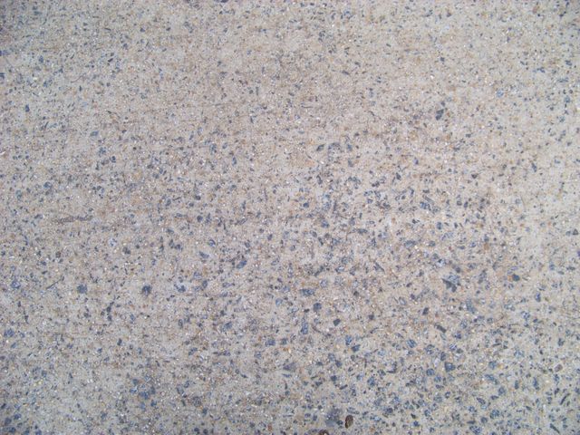 Speckled concrete surface featuring small embedded pebbles offering detailed texture. Ideal as background for construction-related graphics, urban designs, or as a texture layer in graphic design projects.