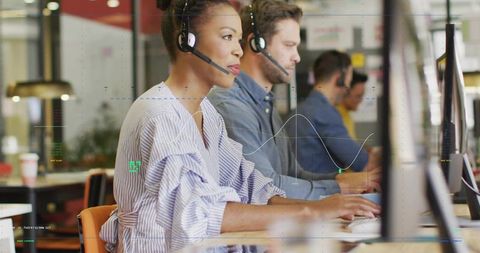 Call center team working in open office wearing headsets typing on desktop computers