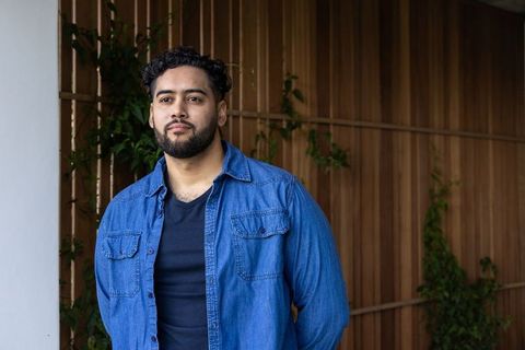 Contemplative man wearing denim shirt standing by wood-paneled entry with climbing vines