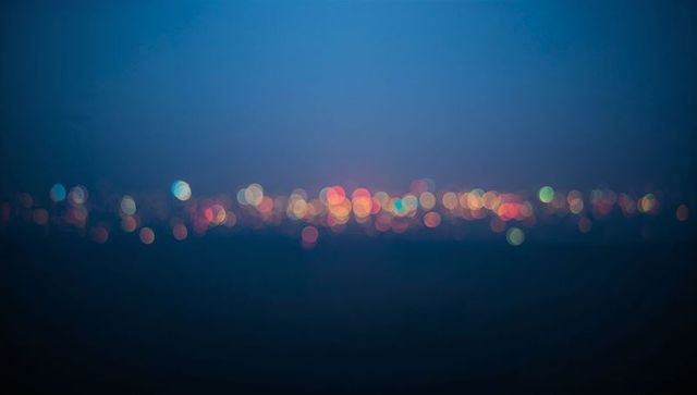 Glowing bokeh city lights along distant night horizon with deep blue gradient and soft blur