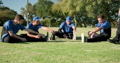 Community sports team stretching together on grass field wearing blue jerseys and caps