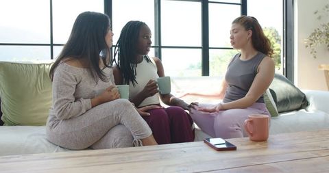 Friends having heartfelt coffee conversation on couch in bright living room