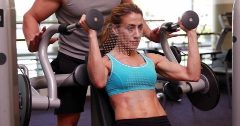 Woman performing seated machine shoulder press with trainer spotting and guiding