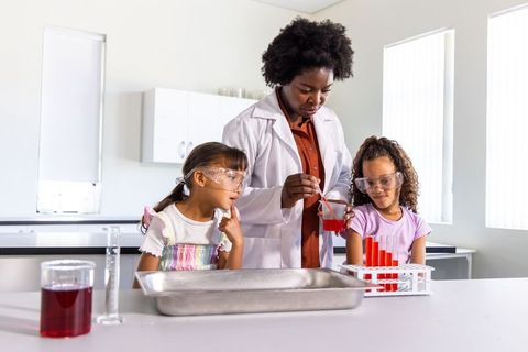 African american teacher guiding young students pouring red liquid during science experiment