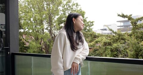 Adult woman leaning on balcony railing looking contemplative with courtyard greenery