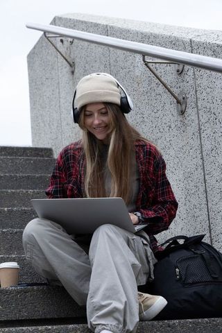 Student studying on campus steps with laptop, headphones and coffee
