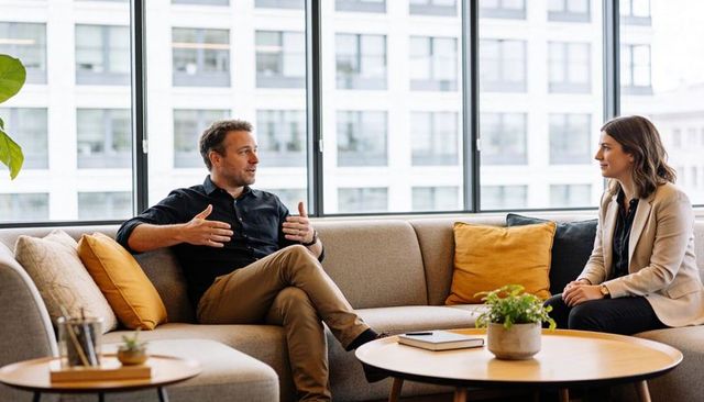 Discussing strategy on office lounge sofa, man gesturing and woman listening attentively