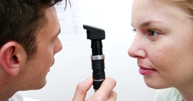 Optometrist carefully examining eyes of a female patient using an otoscope. Useful for medical articles, vision care promotions, picturing doctor-patient interactions, and medical equipment features.