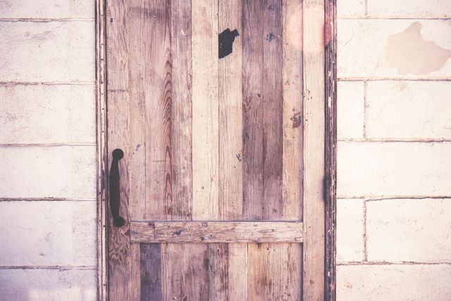 A close-up of a rustic wooden door set in a white brick wall, featuring a black metal handle. This image is perfect for blogs on home renovation, DIY projects, farmhouse decor, and architectural design. Great for use in marketing materials related to rustic home decor, lifestyle, and aesthetic inspiration.