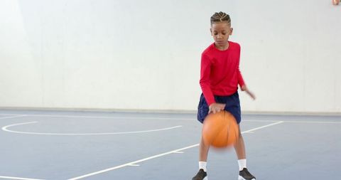 African American boy dribbling basketball on indoor court practicing control and focus