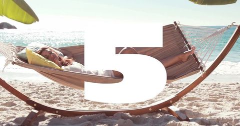 Relaxing woman lounging in hammock on sunlit tropical beach with turquoise ocean view