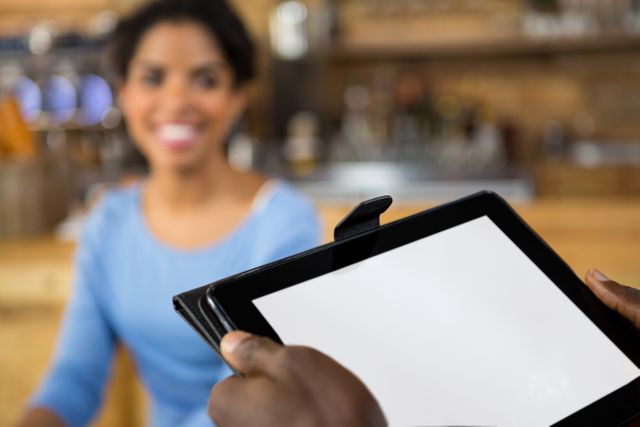 Cropped image of barista hands holding digital tablet with customer in background in cafe